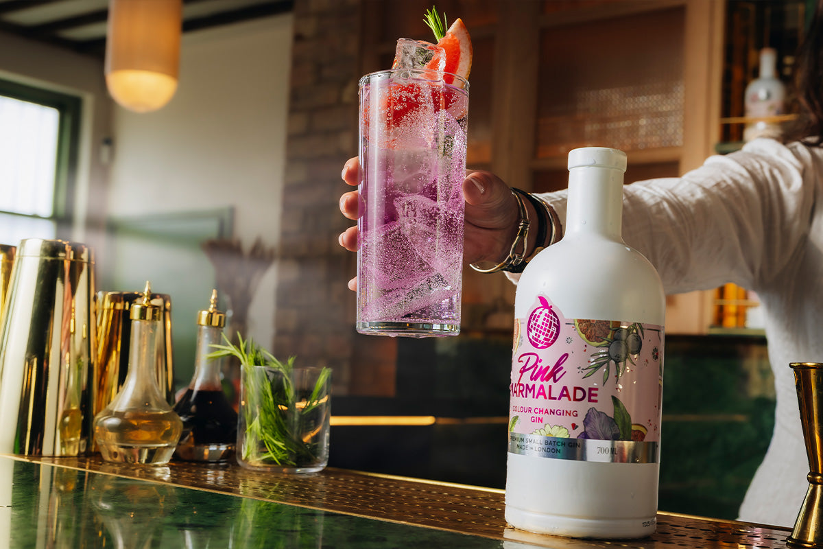 Pink Marmalade Gin on a bar with woman's hand holding a pink gin and tonic cocktail with grapefruit garnish